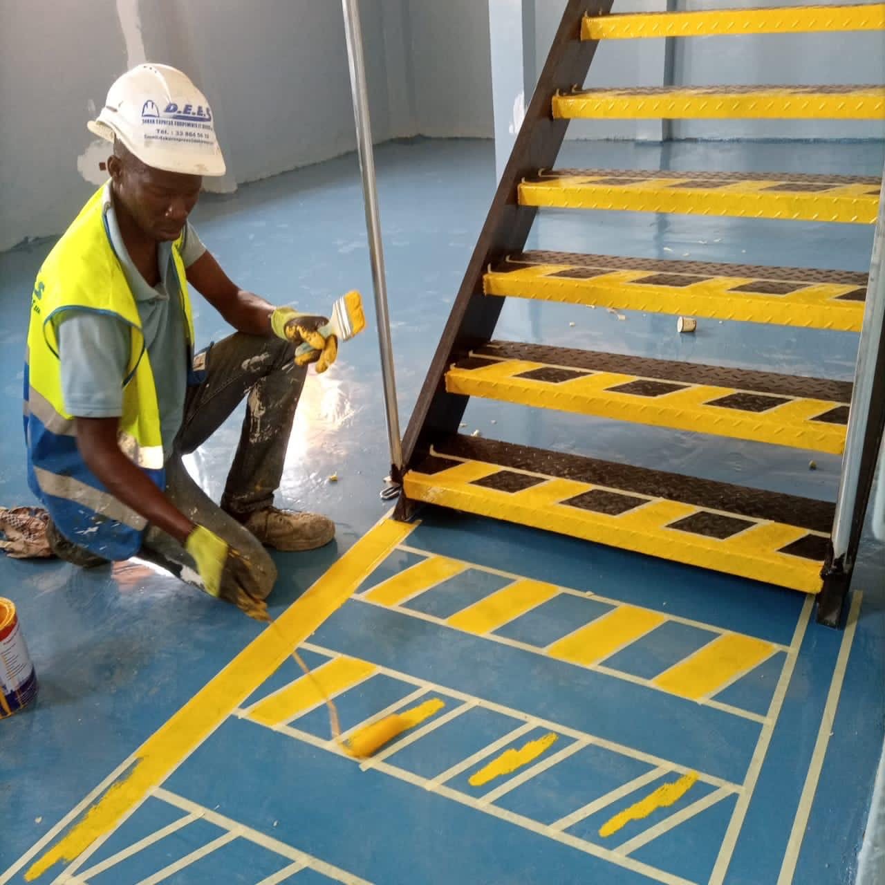 Compagnon DEES traçant un marquage antidérapant jaune au pied d'un escalier